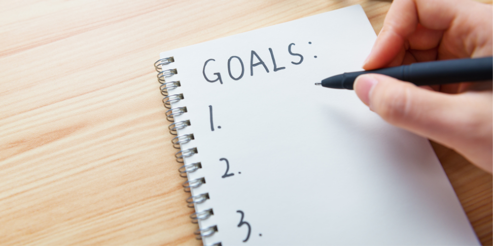 person writing goals on a notebook