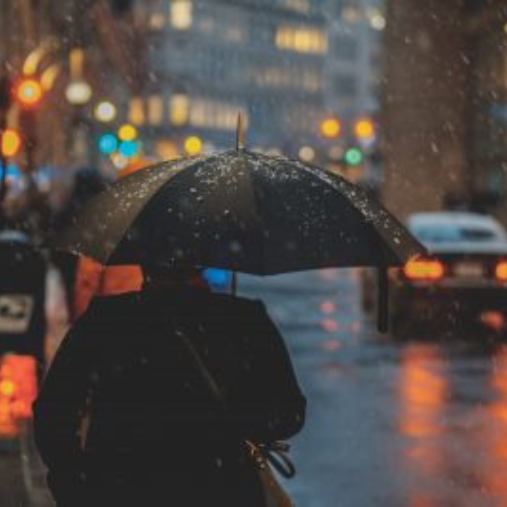 person walking down a darkened city street with an umbrella in the rain